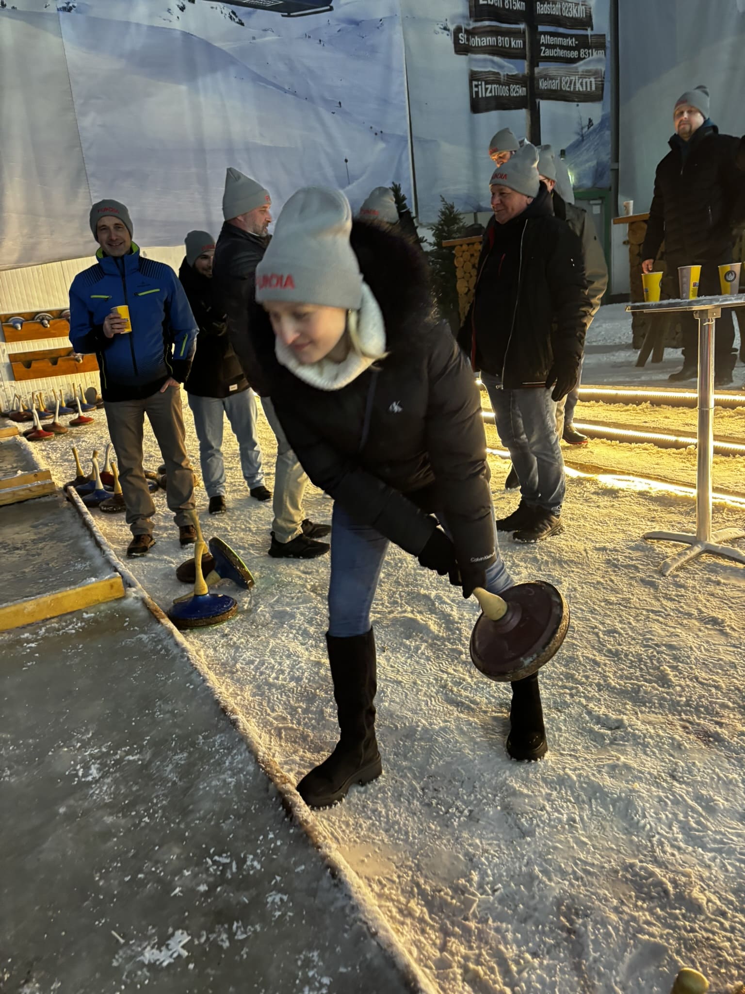 Eine Mitarbeiterin konzentriert sich beim Eisstockschießen im Alpenpark Neuss, während Kollegen im Hintergrund zuschauen.