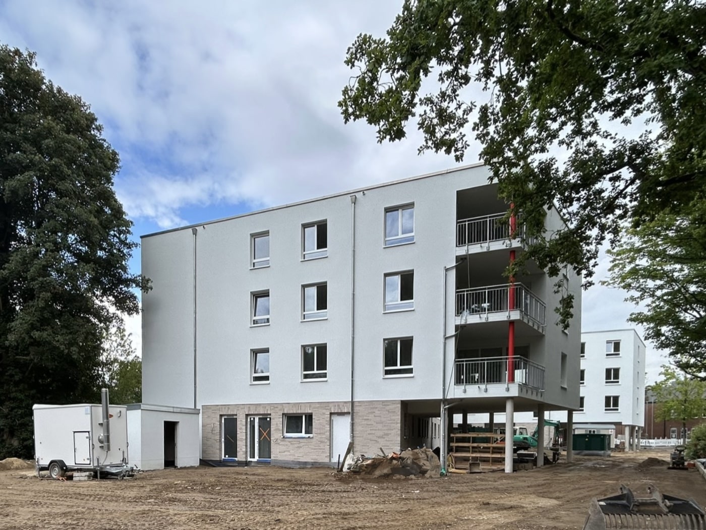 Visualisierung eines modernen Bürogebäudes an einer großen Kreuzung. Der Gebäudekomplex besteht aus einem weißen Eckgebäude mit Rundbögen und einem längeren Flügel mit vertikalen Fassadenelementen. Autos und Fußgänger auf der Straße, blauer Himmel mit Wolken.